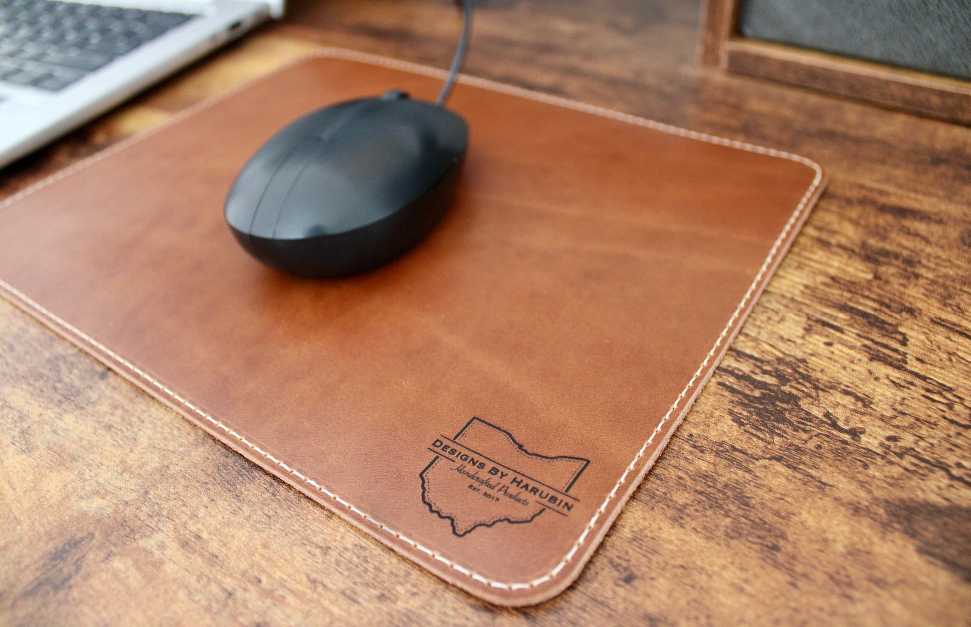 Wheat leather mousepad with cream thread laser engraved with a business logo in the bottom right hand corner.